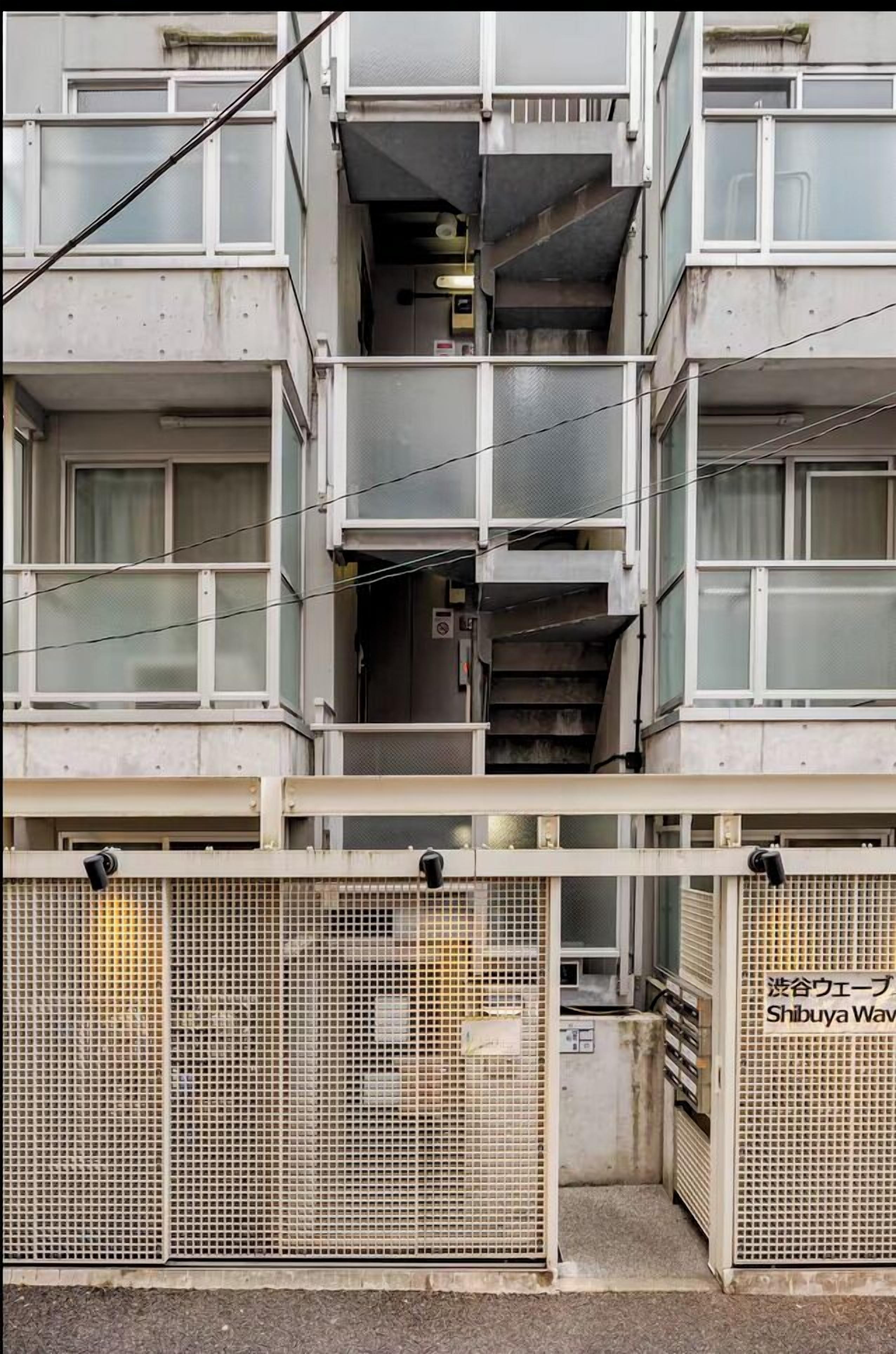 Un immeuble à plusieurs étages doté d’un escalier central, de portails en treillis métallique et d’une enseigne en japonais.