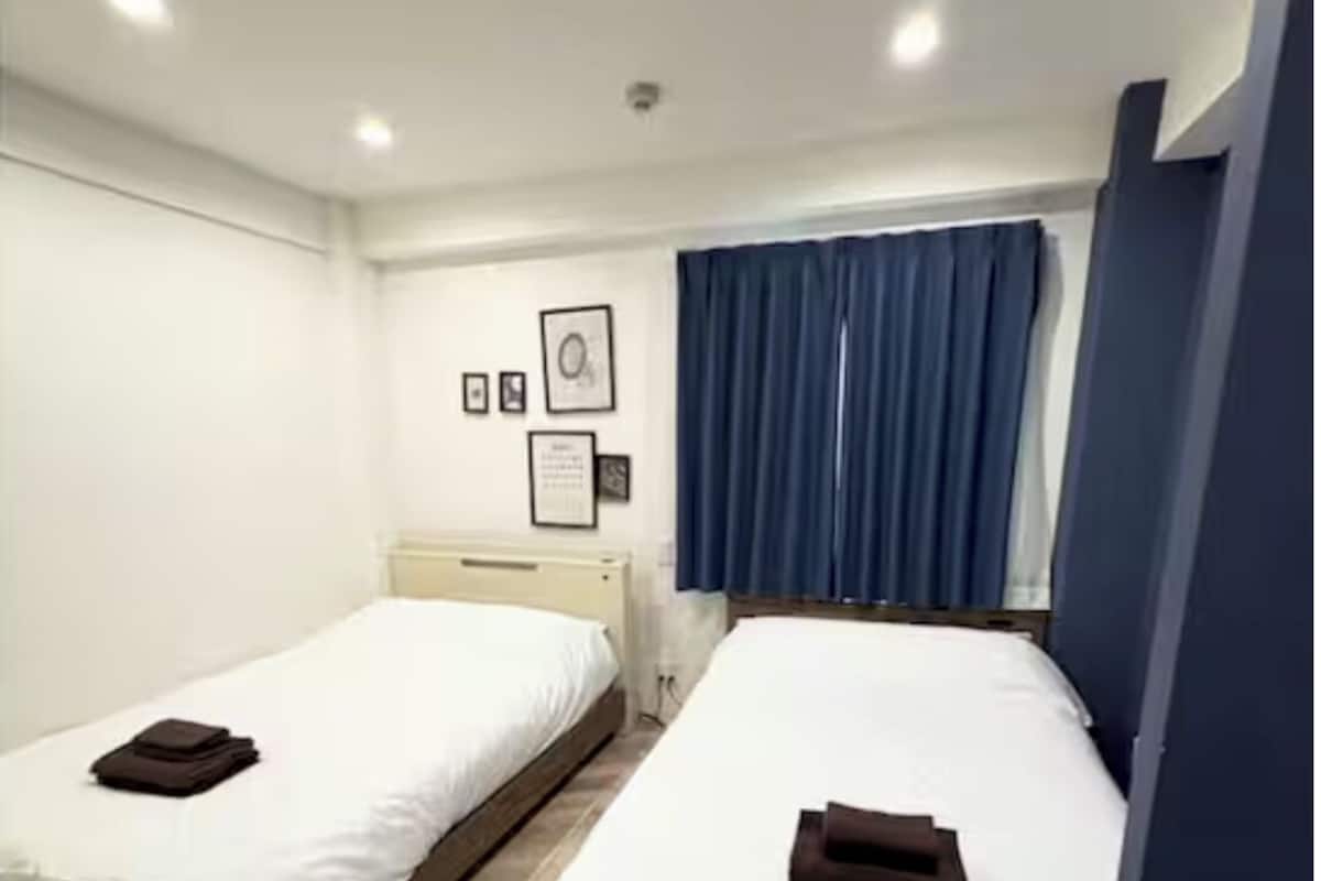 A room with two single beds, a nightstand, a wall-mounted picture, and a window with curtains.