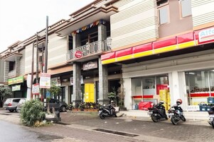 Un edificio con puerta amarilla, balcón y escaparate con toldo rojo y amarillo.