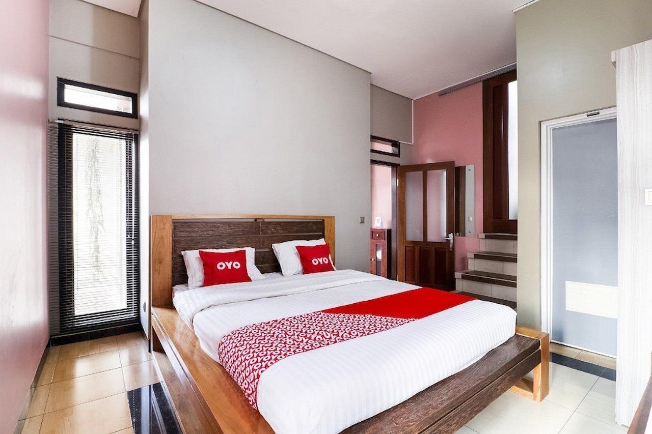 A modern hotel room with a large bed, a wooden headboard, and a red and white patterned bedspread.