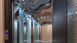 An elevator with reflective glass doors, a digital display, and a checkered floor pattern. - Classic Hotel by Athens Prime Hotels (Athens)