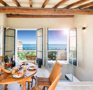 A dining area with a table set for breakfast, overlooking a balcony with a view of the sea.