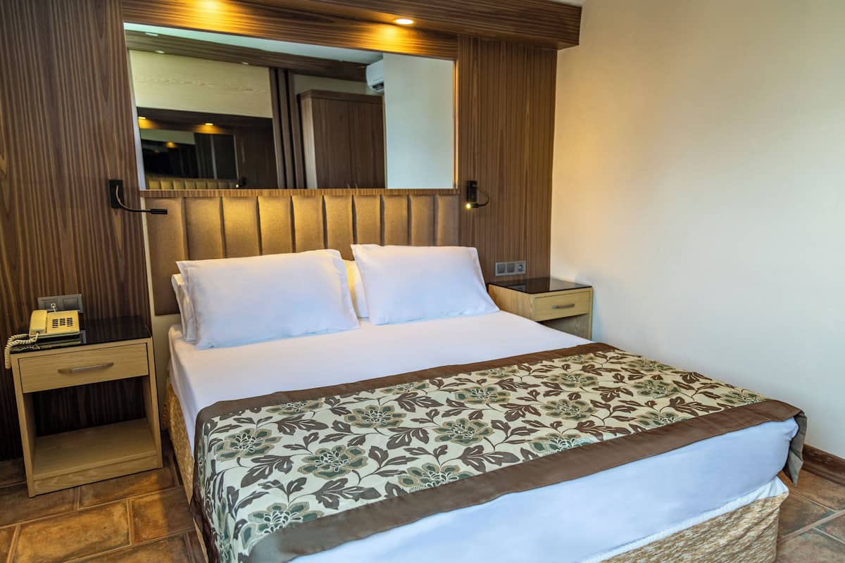 Une chambre d’hôtel avec un grand lit, une table de chevet avec un téléphone, un miroir et une tête de lit en bois.