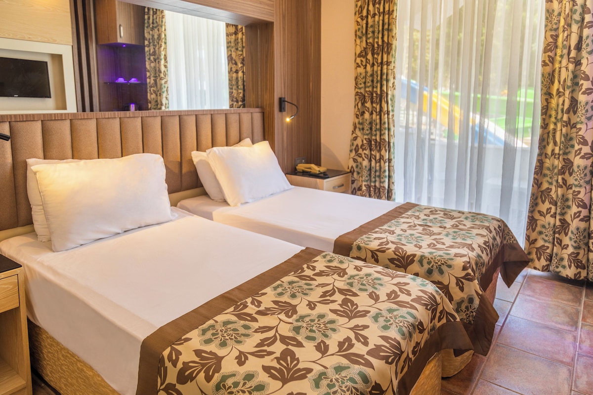 A hotel room with two beds, a TV, and a window with curtains.
