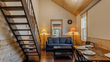 A loft-style room with a wooden staircase, a sofa, a dining table set with plates and glasses, and a lamp.