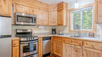 A kitchen with wooden cabinets, stainless steel appliances, a window, and a view of trees.