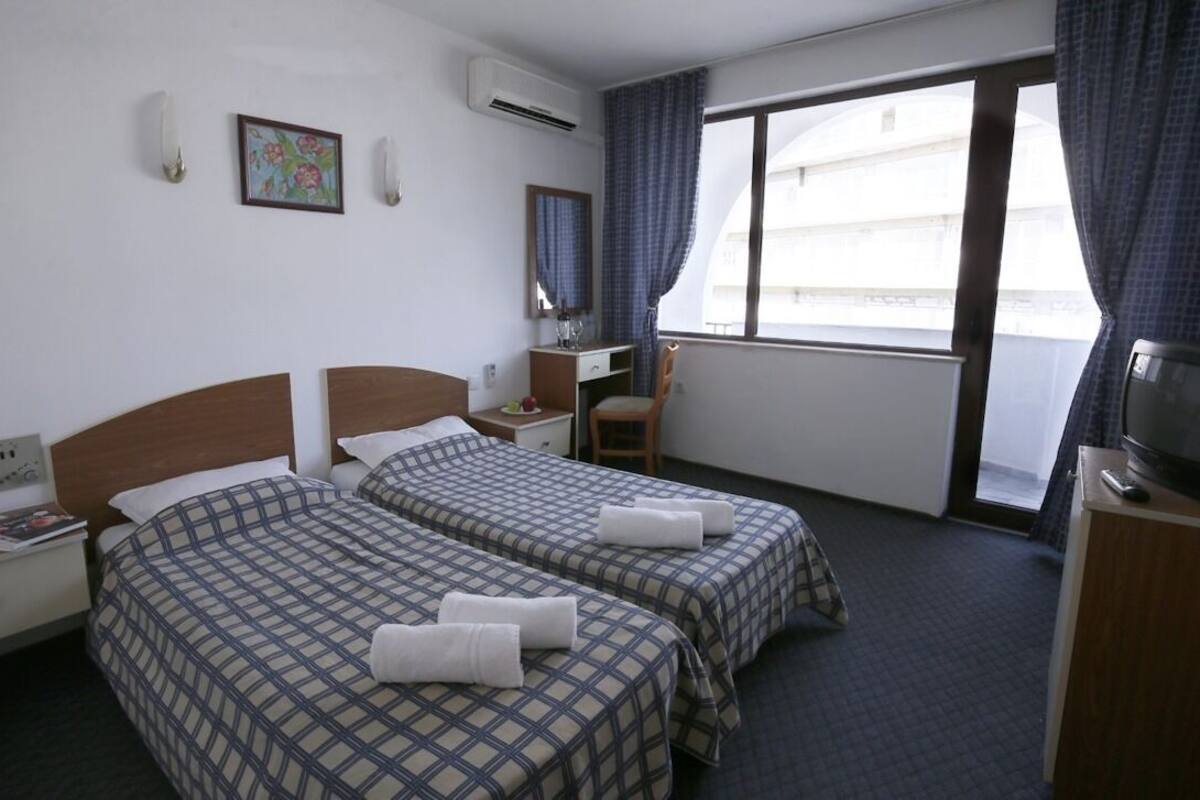 A hotel room with two beds, a desk, a chair, a TV, and a window with curtains.