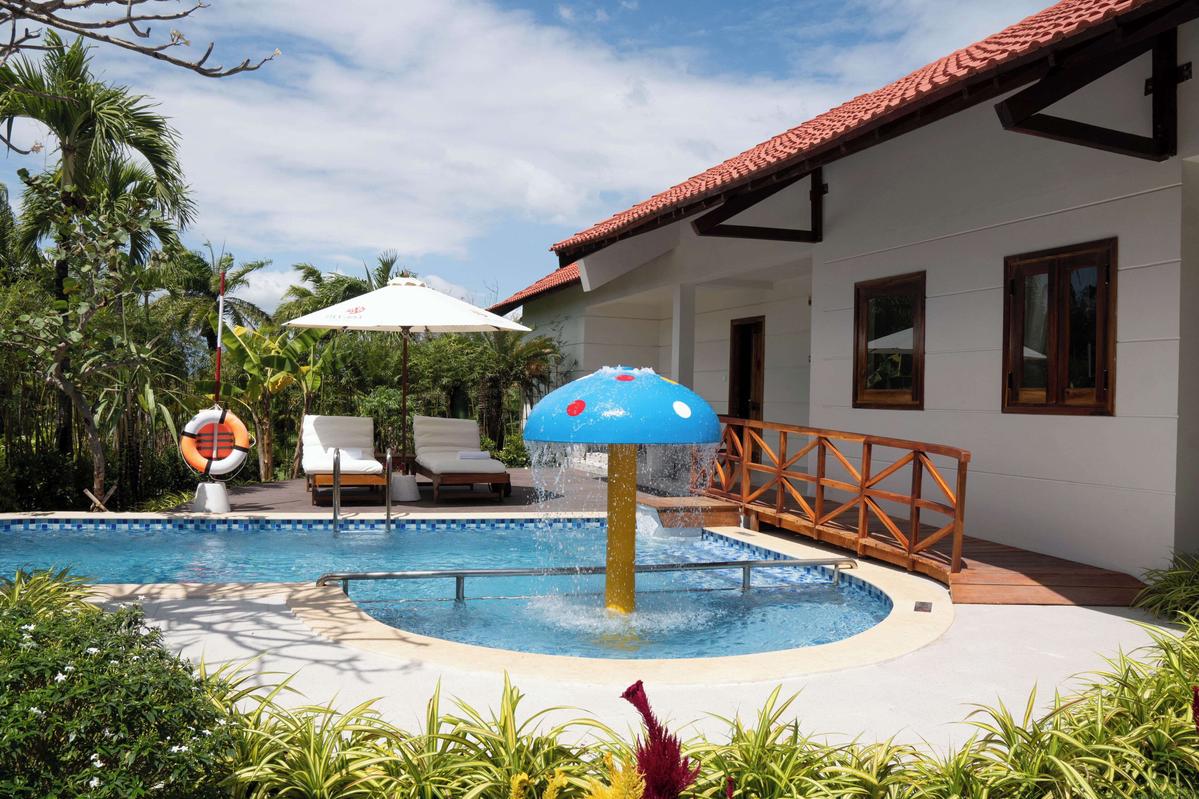 Piscina com fonte de água, espreguiçadeiras e uma palmeira.