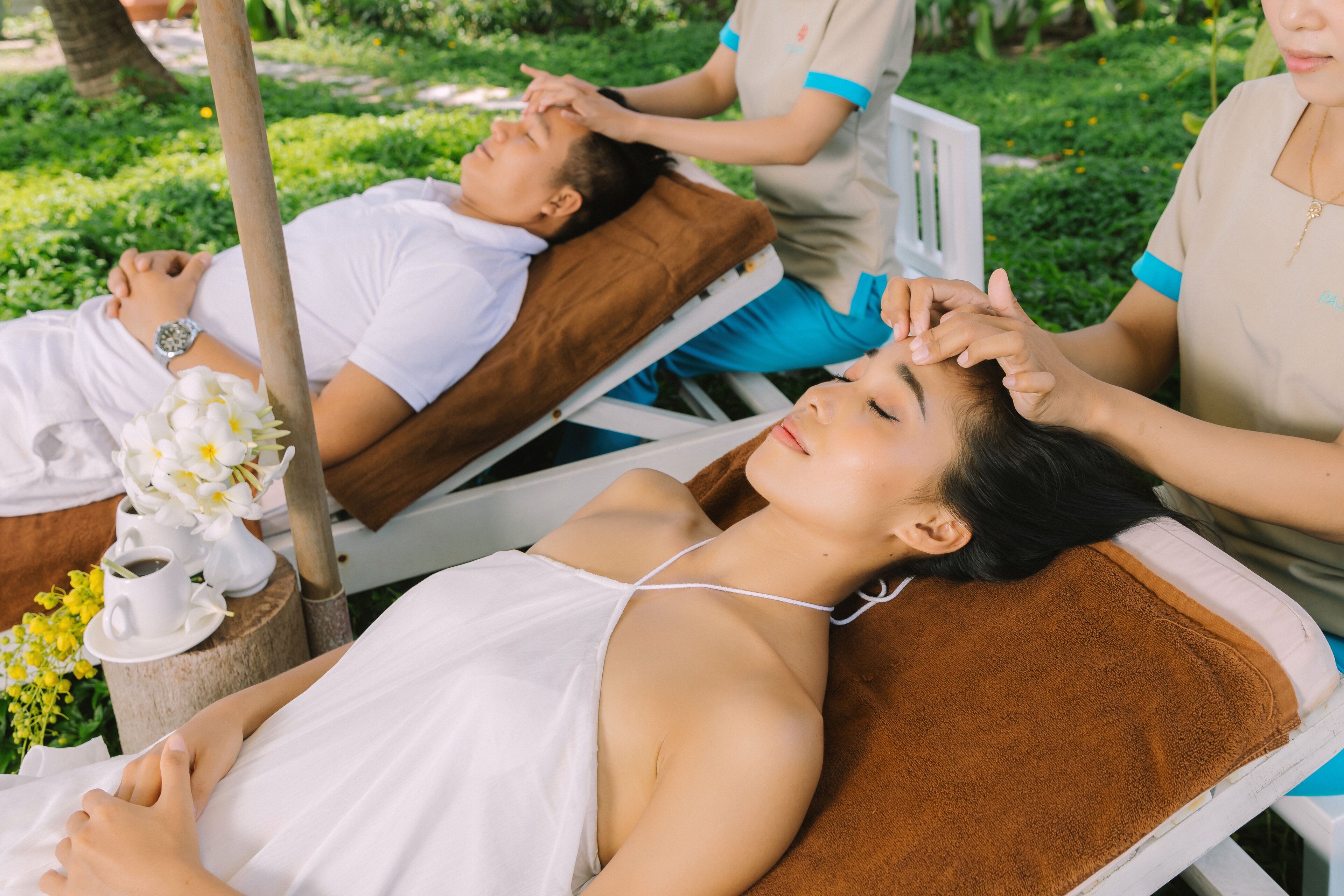 A spa treatment area with two clients lying on treatment beds, one receiving a head massage.