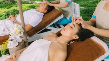 A spa treatment area with two clients lying on treatment beds, one receiving a head massage.