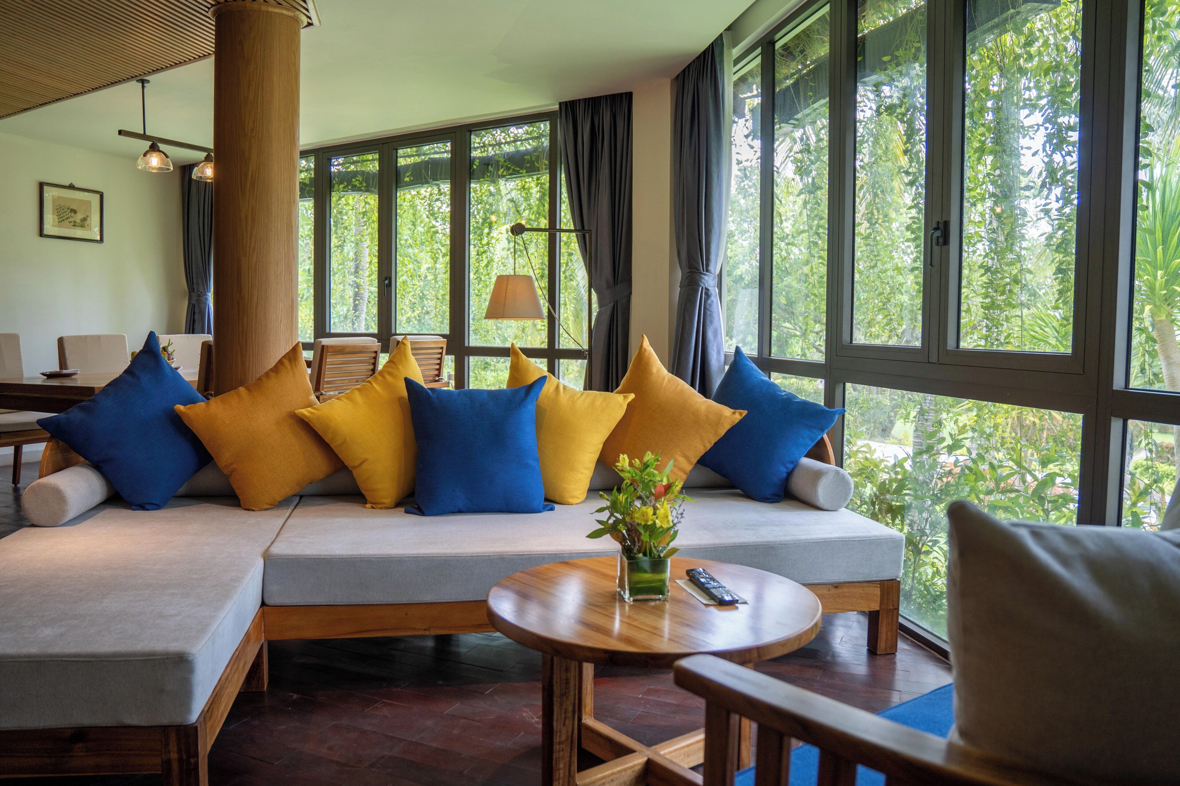 Un salon moderne avec un canapé d’angle, une table basse et une vue sur la verdure grâce à de grandes fenêtres.