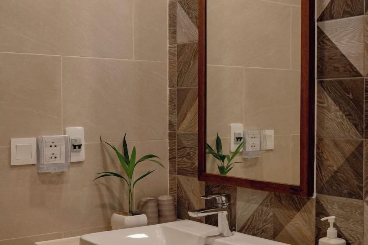 Un baño con un lavamanos blanco, un espejo y una planta en maceta.