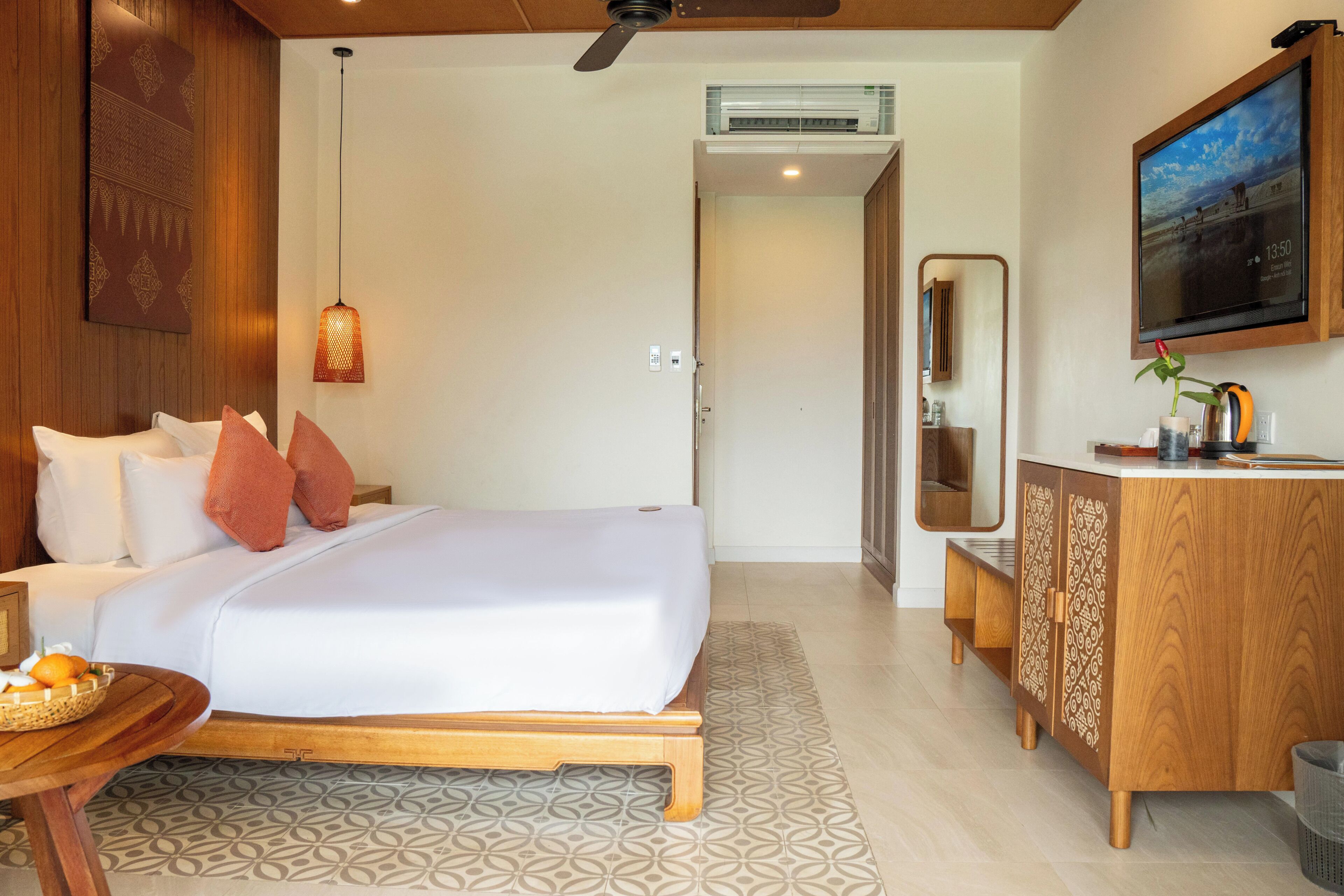 A hotel room with a bed, bedside table, and a wooden cabinet with a mirror.
