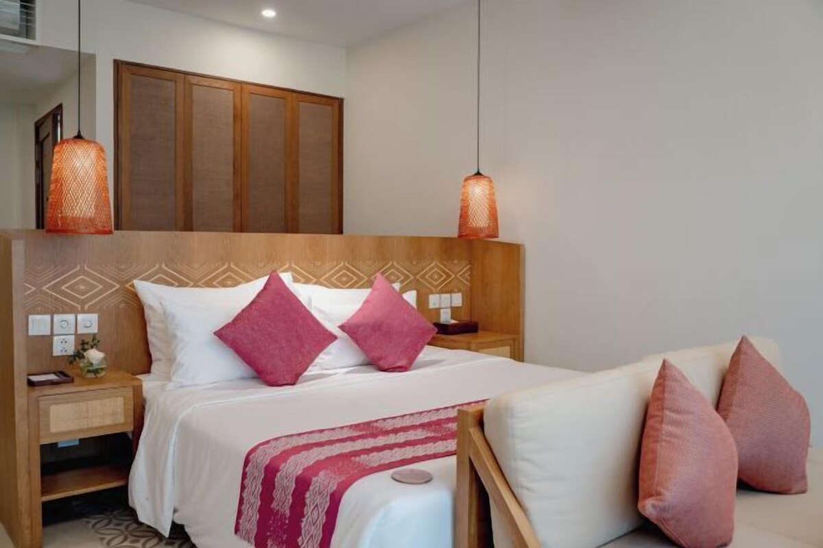 A hotel room with a wooden headboard, two bedside tables, a bed with white bedding and pink pillows, and hanging orange lamps.