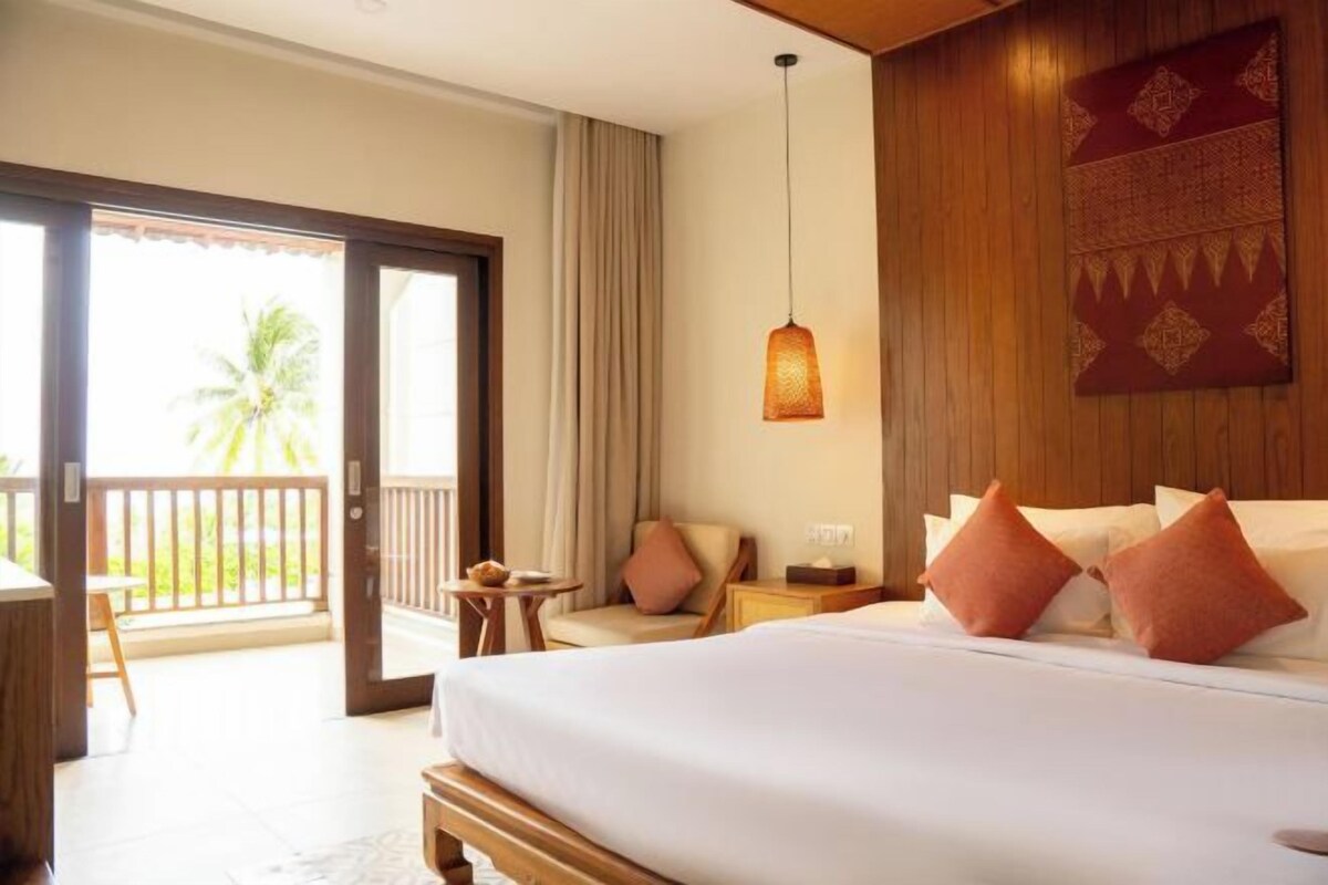 A hotel room with a bed, a balcony, a small table, and a hanging light fixture.