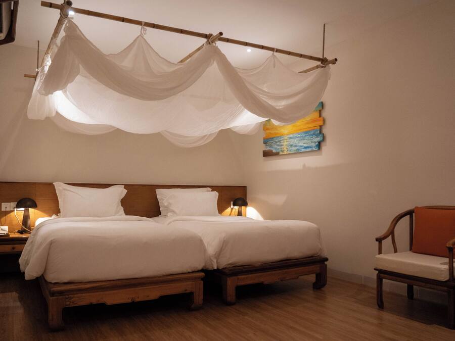 Un lit double avec une tête de lit en bois, deux lampes de chevet, une chaise et un tableau accroché au mur.