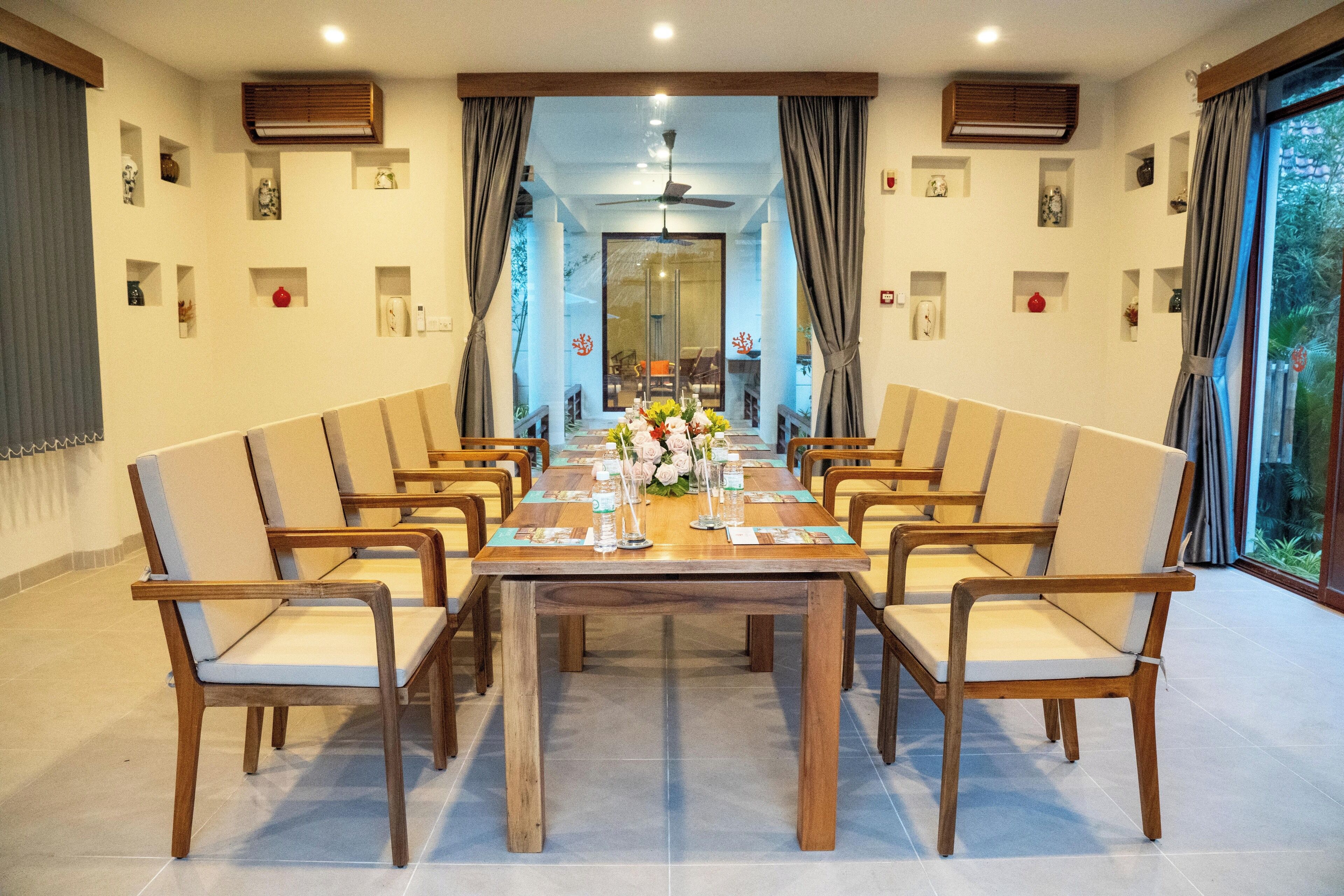 A dining area with a long wooden table, multiple chairs, and a view through a glass door to an outdoor area.