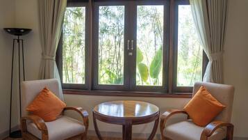 Una habitación con dos sillas de madera con cojines, una mesita de madera y un ventanal con cortinas.