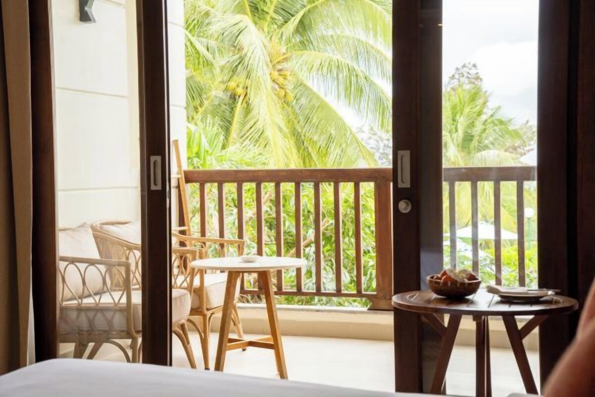 Habitación con balcón, mobiliario de mimbre y vista a palmeras.