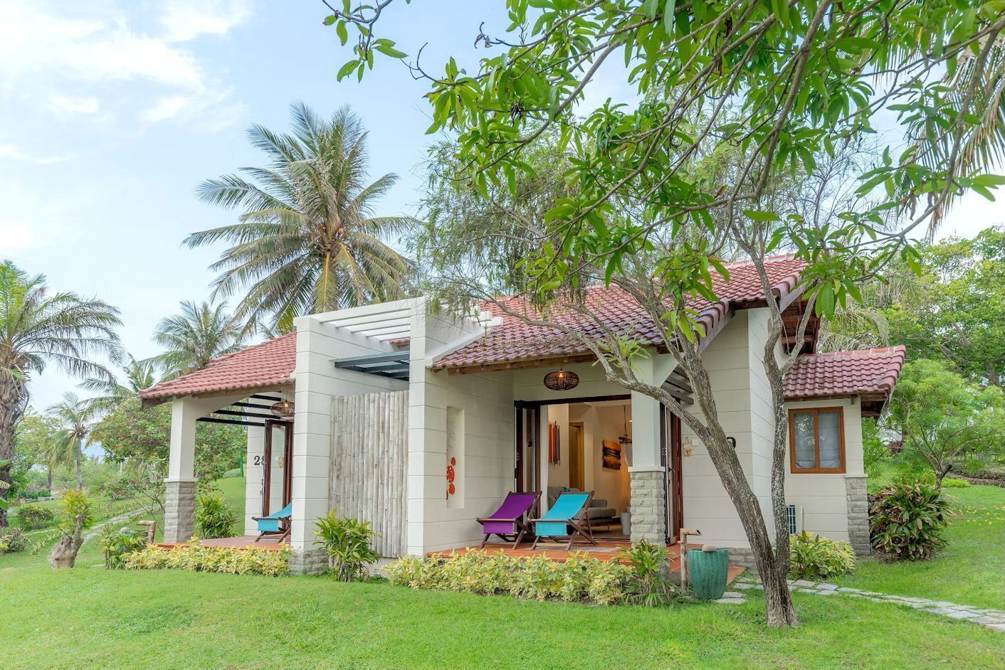 Uma casa de dois andares com varanda coberta, um pequeno jardim e palmeiras.
