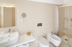 Un baño moderno con un espejo grande, dos lavamanos, un bidé y una ducha con mampara de vidrio.