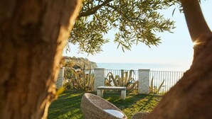 A patio with wicker chairs, a stone bench, and a view of the sea. - Tui Blue Tropea – Baia di Riaci Resort (Santa Domenica)