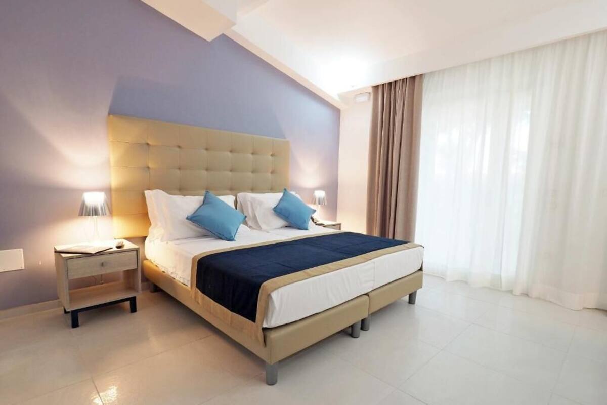 A modern hotel room with a large bed, a nightstand, and a window with curtains.