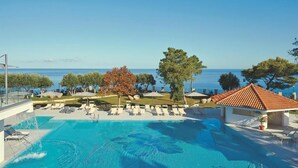 A swimming pool with lounge chairs and umbrellas, surrounded by trees and a view of the sea. - Tui Blue Tropea – Baia di Riaci Resort (Santa Domenica)