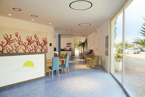 Un hall de hotel con zona de comedor, mostrador de recepción y un amplio ventanal con vistas a la calle.