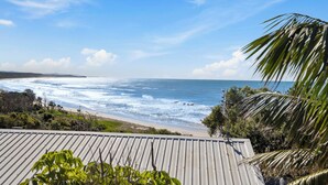 Une vue sur la côte, prise depuis un quartier résidentiel, avec un toit en métal, des palmiers et une plage en arrière-plan.