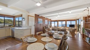 Une vaste salle à manger avec une grande table dressée pour le repas, un plancher en bois et une vue sur l’océan grâce à de grandes fenêtres.