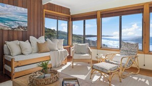 Une pièce chaleureuse avec un banc en bois, deux chaises et une vue sur l’océan.