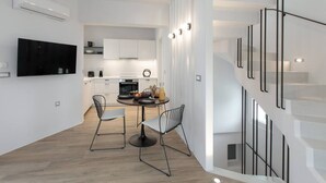 Una cocina moderna con armarios blancos, un televisor de pantalla plana y una zona de comedor con dos sillas y una mesa.