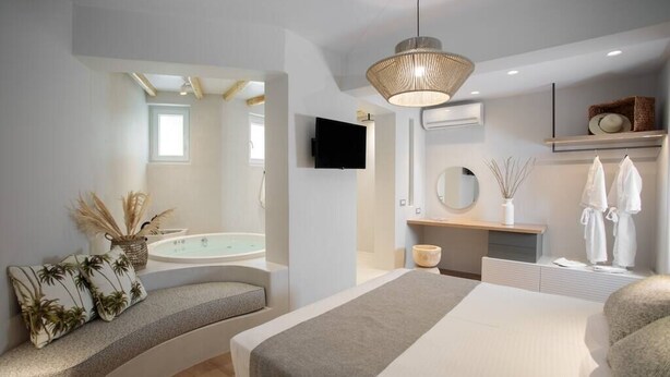 Un dormitorio moderno con una cama grande, un banco integrado, un televisor, una bañera y un espejo.