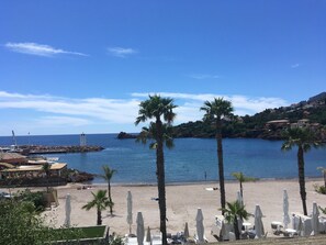 Ein Strand mit Palmen, einem Steg und Gebäuden an einem Hügelhang.