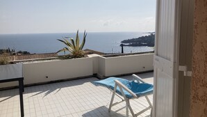 A balcony with a view of the sea, a blue chair, and a large plant. - Séjour de Rêve sur la Côte D'azur (Théoule-sur-Mer)