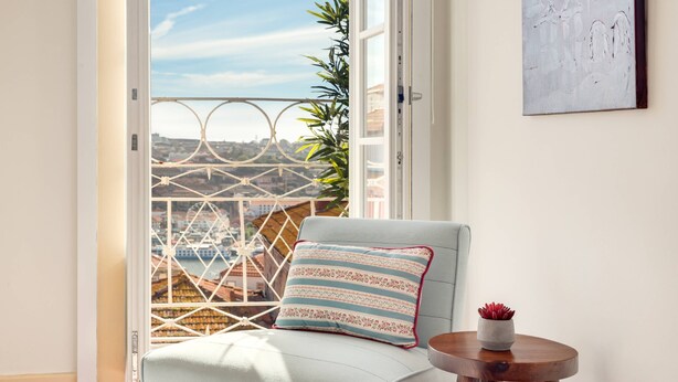Un balcone con una sedia, un tavolino, una ringhiera e vista sugli edifici.