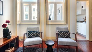 Un soggiorno moderno con due poltrone, un tavolino da caffè e una libreria. Ampie finestre offrono luce naturale e vista sulla città.