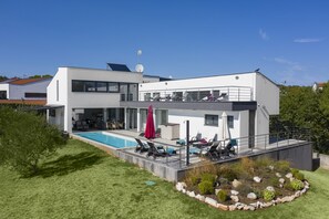 Een modern huis met twee verdiepingen, een zwembad, buitenmeubilair en een tuin.