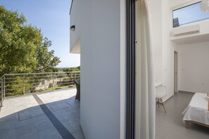 Une chambre d’hôtel moderne dotée d’un balcon, d’un coin repas et offrant une vue sur les arbres et un paysage lointain.