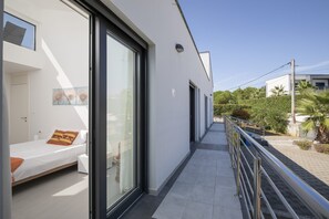 Une chambre d’hôtel moderne avec un balcon, un lit avec des oreillers, une fenêtre et une porte.