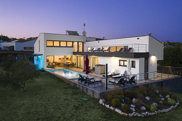 A modern two-story house with a swimming pool, outdoor seating, and a well-maintained garden.