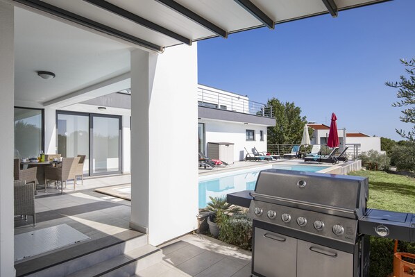A modern outdoor patio with a pool, a grill, and a dining area with outdoor furniture.