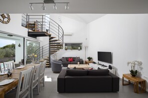 Ein moderner Wohnraum mit Wendeltreppe, Essbereich, Sofa und Fernseher.