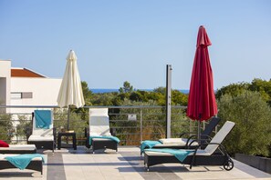 A rooftop terrace with lounge chairs, a table, and umbrellas.