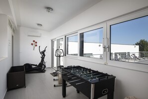 Een moderne kamer met een tafelvoetbaltafel, fitnessapparatuur en grote ramen.
