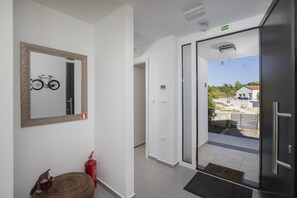 Un intérieur moderne avec un vélo accroché au mur, un extincteur et une vue sur un espace extérieur, visible à travers une porte vitrée.