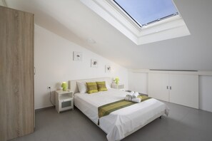 Een moderne slaapkamer met dakraam, een bed met witte beddengoed en groene accenten, een nachtkastje met een lamp en een kledingkast.