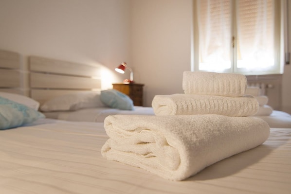 A neatly made bed with folded white towels, a bedside lamp, and a window with curtains.