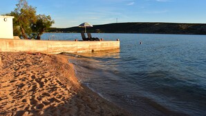 A beach with a concrete barrier, lounge chairs, and a small umbrella. - Villa Vita (Novalja)